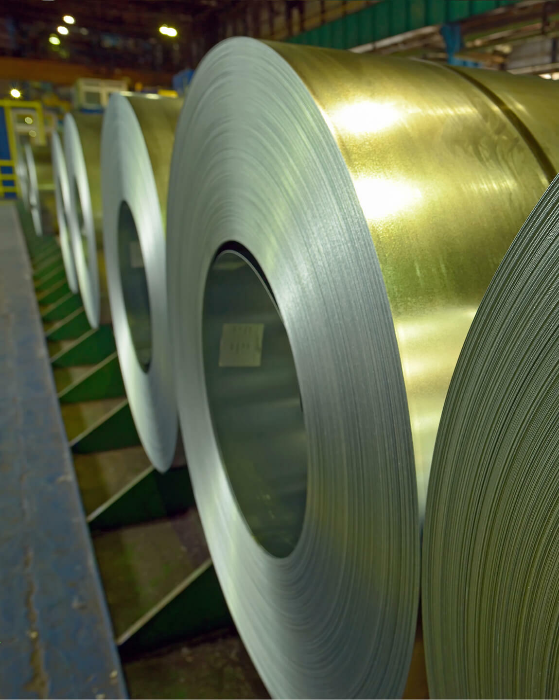 Large rolls of metal sheet material lined up in an industrial facility for nickel alloy cleaner
